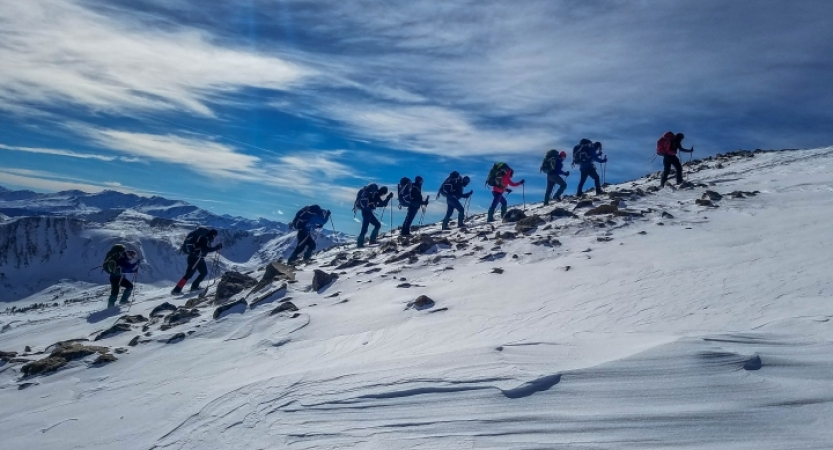 A group of gap year students hike along a snowy ridge. There are mountains in the background. 